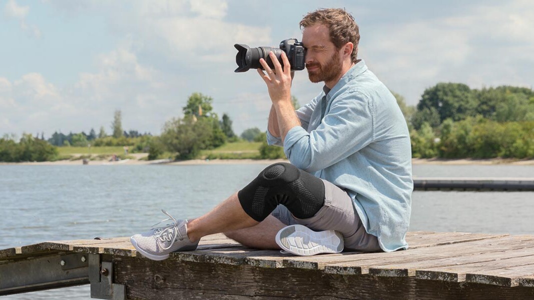 En fotograf sidder på en bro. Han har en Juzo-knæbandage på En fotograf sidder på en bro. Han har en Juzo-knæbandage på