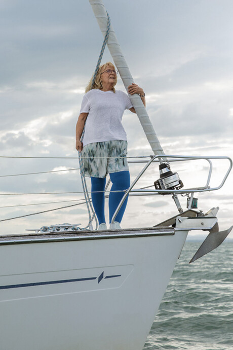 A woman with lymphoedema is standing on the deck of a boat. She is wearing blue compression stockings