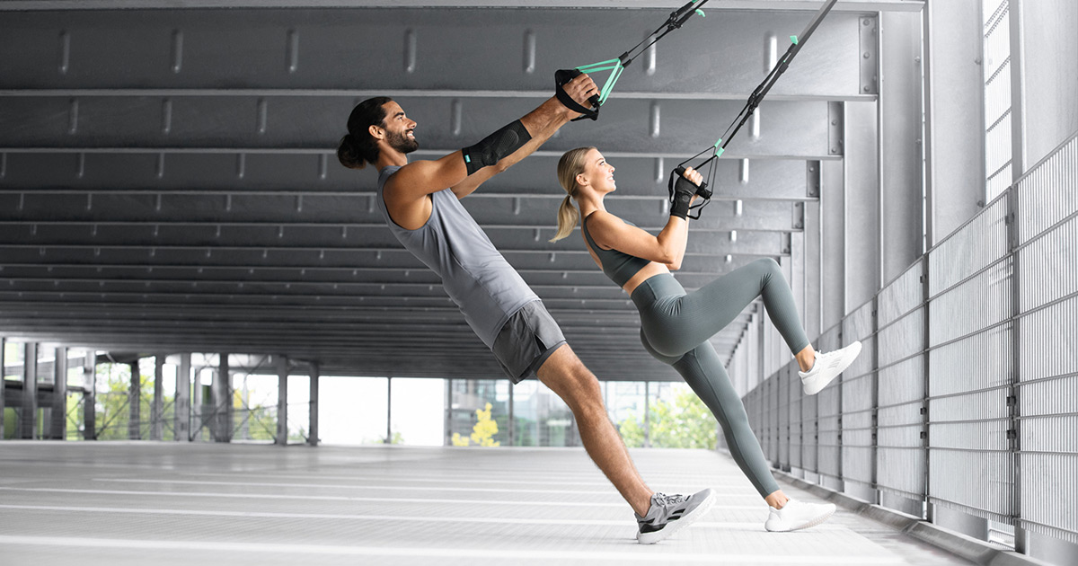 Un homme et une femme s'entraînent dans un parking souterrain avec une sangle TRX Un homme et une femme s'entraînent dans un parking souterrain avec une sangle TRX