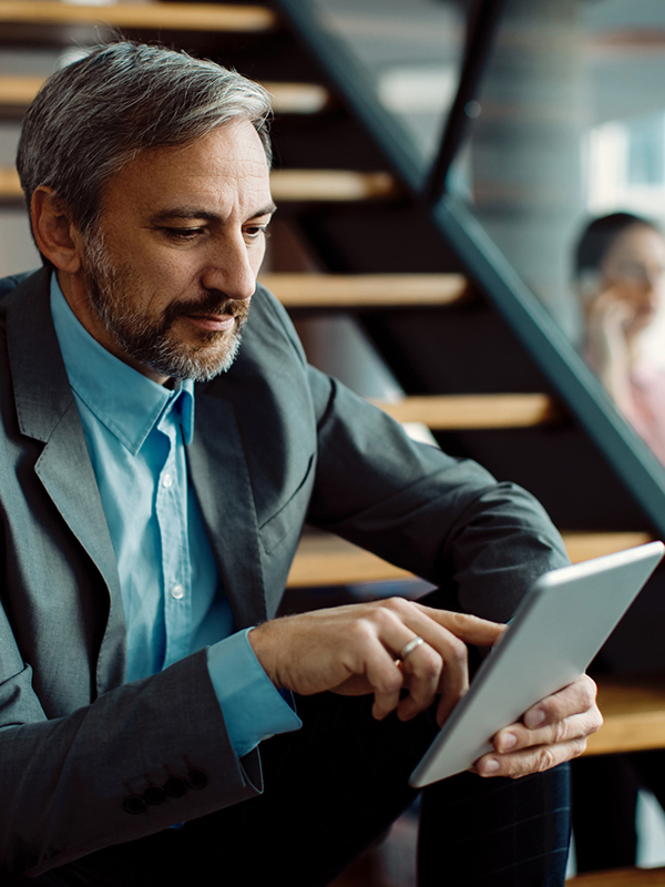 A man in a suit is sitting on a flight of stairs, tapping away on a tablet A man in a suit is sitting on a flight of stairs, tapping away on a tablet