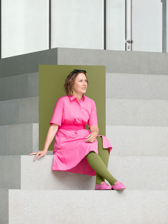 A woman in a pink dress sits on large steps wearing a Pure Olive compression garment