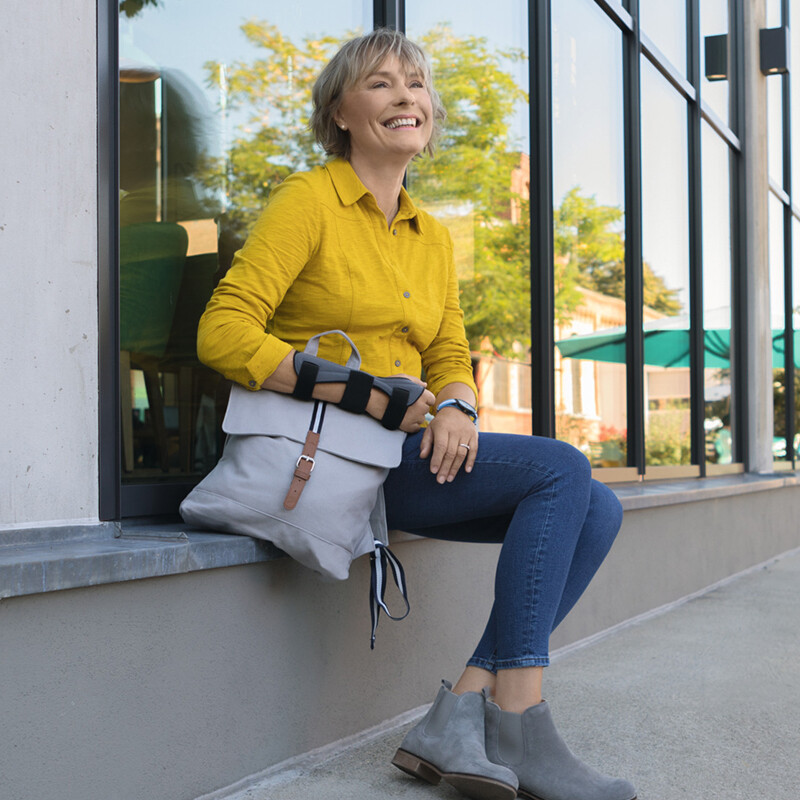 A woman is sitting on a windowsill, holding her bag. She is wearing a wrist brace