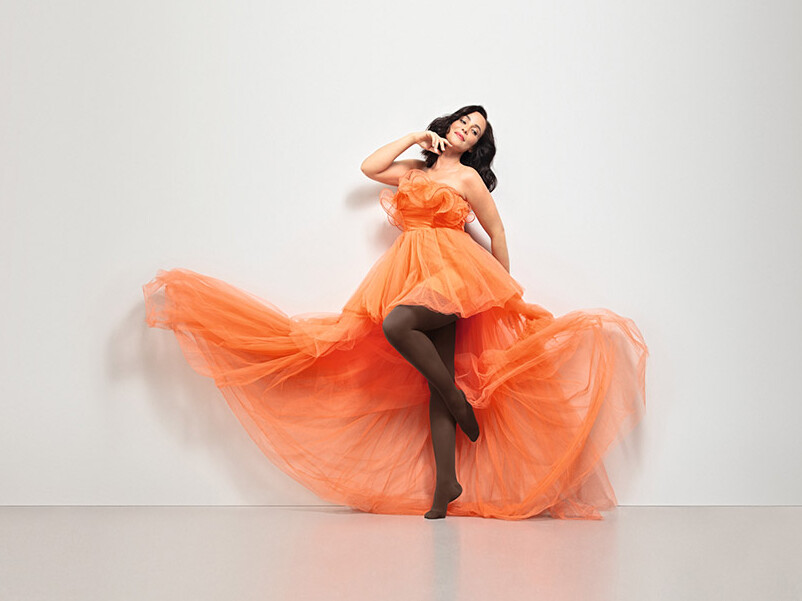 A woman is wearing an orange tulle dress and Juzo Inspiration in cocoa