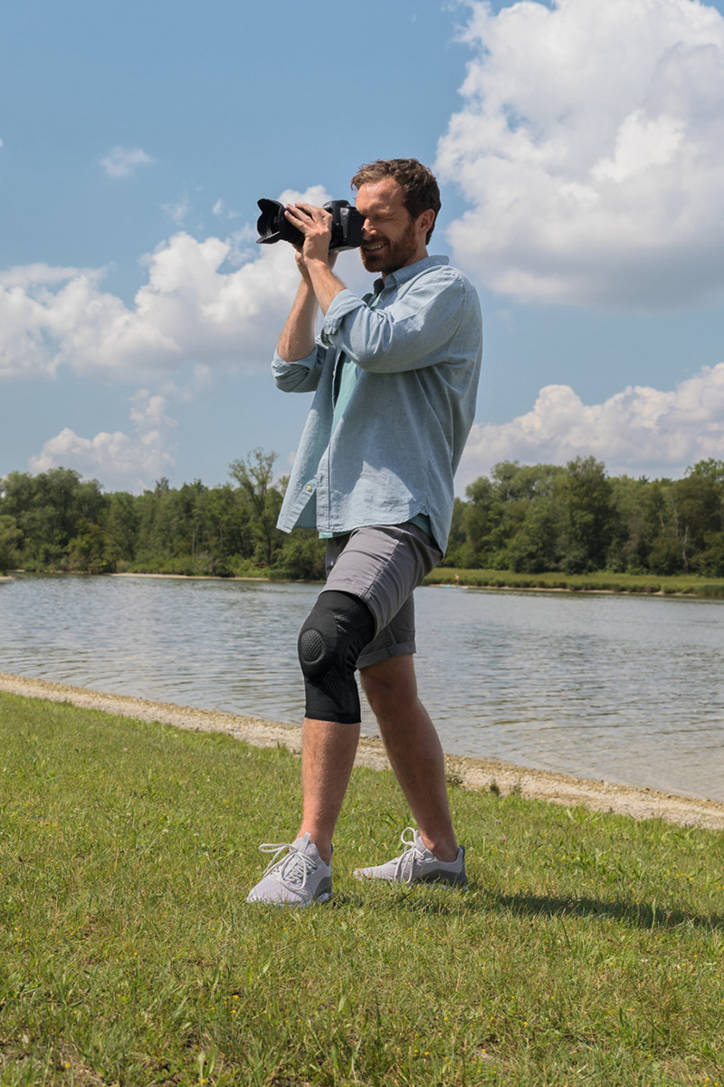 A man is taking photographs in the countryside. He is wearing a knee brace.