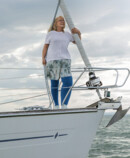 A woman with lymphoedema is standing on the deck of a boat. She is wearing blue compression stockings