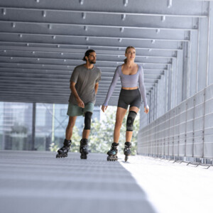Um homem e uma mulher, ambos com uma joelheira, andam de patins numa garagem Um homem e uma mulher, ambos com uma joelheira, andam de patins numa garagem