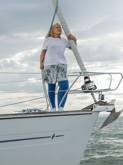 A woman with lymphoedema is standing on the deck of a boat. She is wearing blue compression stockings