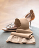 Juzo Soft Sesame lying on a cushion next to a Cinderella shoe