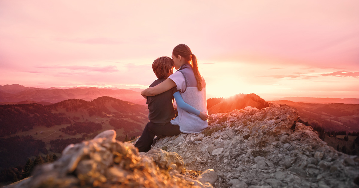 Une mère est assise avec son enfant au sommet d'une montagne. L'enfant porte une manchette de compression. Une mère est assise avec son enfant au sommet d'une montagne. L'enfant porte une manchette de compression.